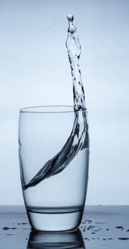 water splashing out of a glass on blue background