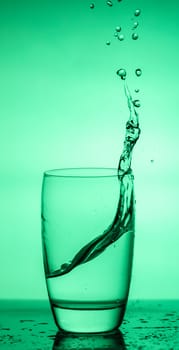 water splashing out of a glass on green background