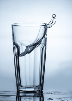 water splashing out of a glass on blue background