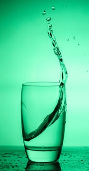 water splashing out of a glass on green background