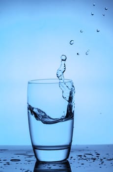 water splashing out of a glass on blue background