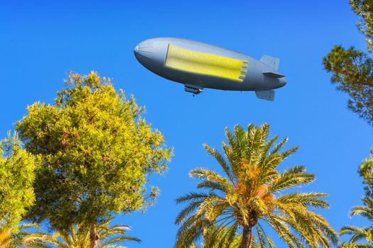 Landscape, tree tops of pines and palm trees on the Mediterranean Sea on Mallorca in Spain. In the sky a zeppelin with banner, copy space.