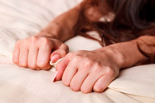 Woman's hands pulling white sheets in ecstasy, orgasm