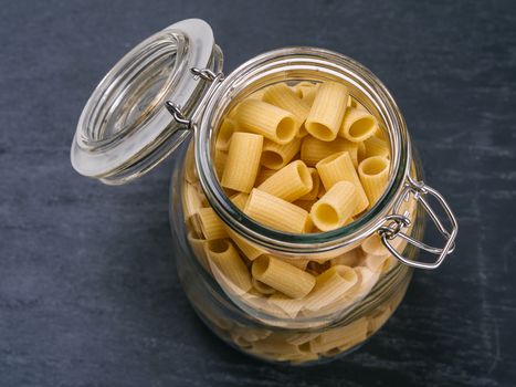 Photo of Mezzi Rigatoni in an open jar on top of a slate background.