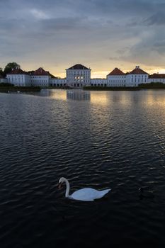 Dramatic scenery of Nymphenburg palace in Munich Germany. Sunset after the sorm. White swan swimming in pond in front of the palace.