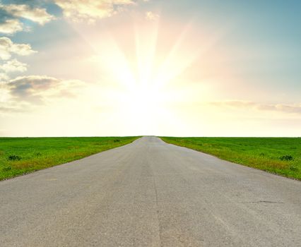 Asphalt road in a grass field against a beautiful sunrise. The concept of success