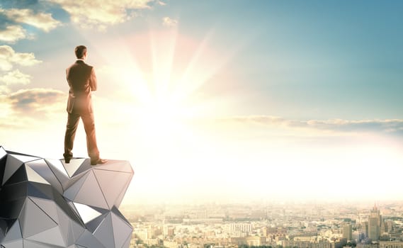 A businessman in a suit stands on an abstract metal construction and looks at the sunrise. Ahead of city landscape