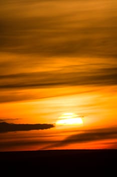 Setting sun in orange sky with clouds.