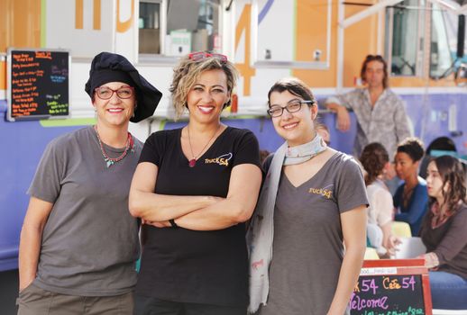 Three smiling food truck entrepreneurs in front of their food truck outdoors