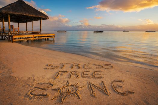 Forground written in the sand "stress free zone" at sunset in Mauritius Island with Jetty silhouette and Fishermen's boats in the background.