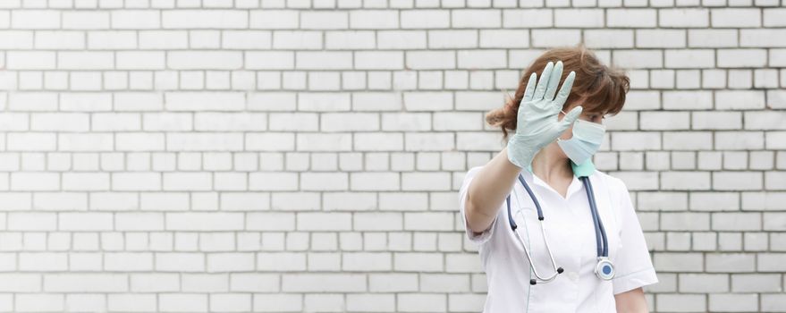 Doctor concept. Close your face with your hands. Medical secrecy. Girl in white medical dressing gown on brick wall background. Photo for your design. Horizontal sheet orientation