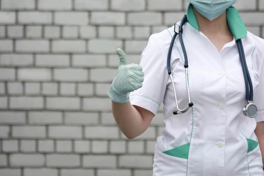Doctor concept. A good result of the operation. Girl in white medical dressing gown on brick wall background. Photo for your design. Horizontal sheet orientation