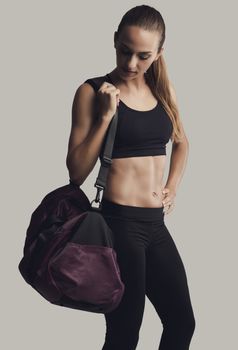 Portrait of sporty young woman posing with a gym bag,  against a gray background