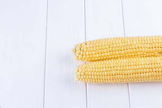 Two raw maize cobs at white wooden table background