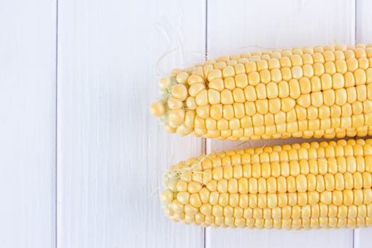 Two raw maize cobs at white wooden table background