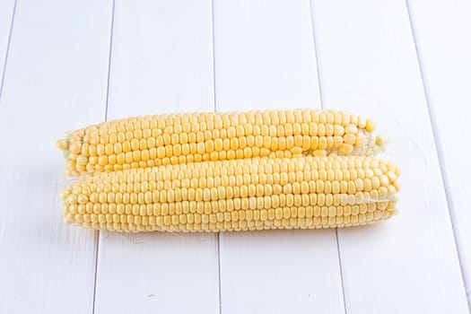 Two raw maize cobs at white wooden table background