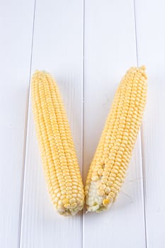 Two raw maize cobs at white wooden table background