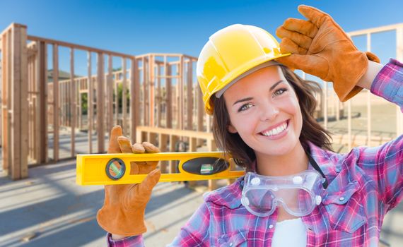 Female Construction Worker Holding Level Wearing Gloves, Hard Hat and Protective Goggles at Construction Site.