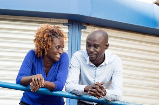 This young couple leaning against a balcony leads their conversation with joy.