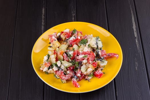 Salad of tomato pepper feta in a yellow plate on a black wooden background