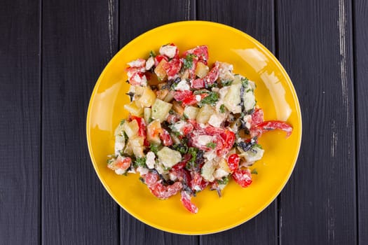 Salad of tomato pepper feta in a yellow plate on a black wooden background