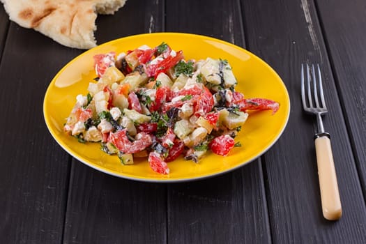 Salad of tomato pepper feta in a yellow plate on a black wooden background