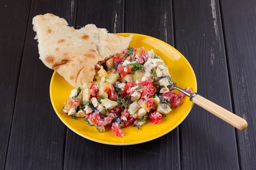 Salad of tomato pepper feta in a yellow plate on a black wooden background