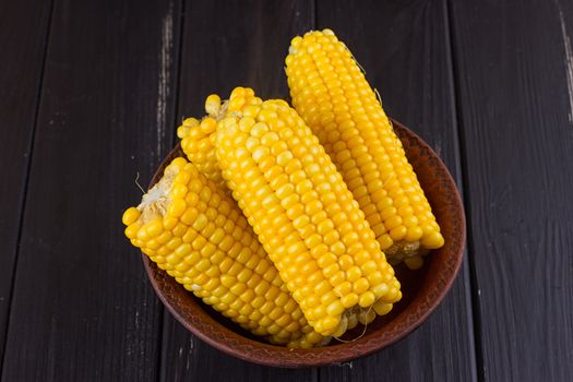 Boiled corn in a bowl on a black wooden background