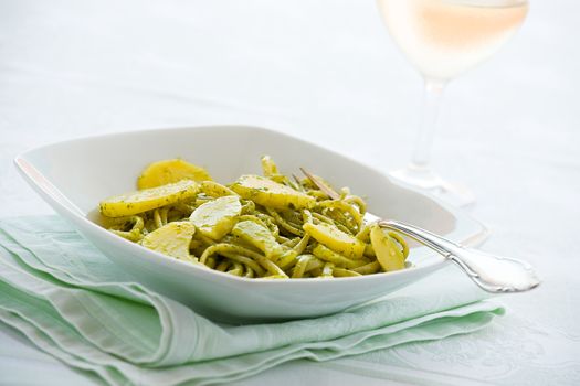 Linguine pasta with pesto genovese and potatoes over a table with fork and white wine glass