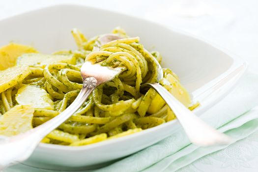 Closeup of linguine pasta with pesto genovese and potatoes over a table with cutlery