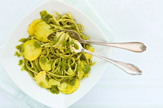 Closeup of linguine pasta with pesto genovese and potatoes over a table with cutlery seen from above