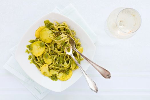 Linguine pasta with pesto genovese, potatoes and white wine glass seen from above