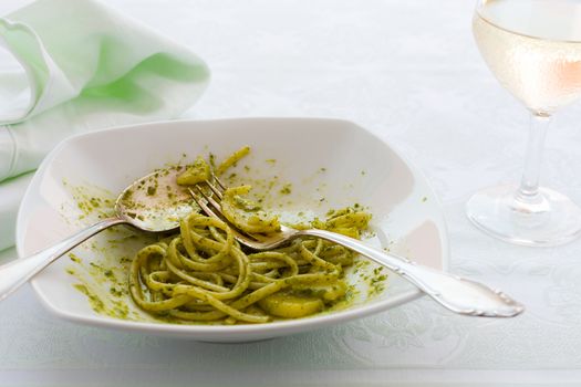 Closeup of eaten linguine pasta with pesto genovese, potatoes and white wine glass