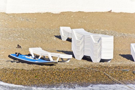 Empty beach with sun loungers and surfboard in summer day