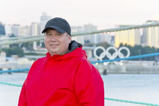 Big fat man in red jacket on embankment background