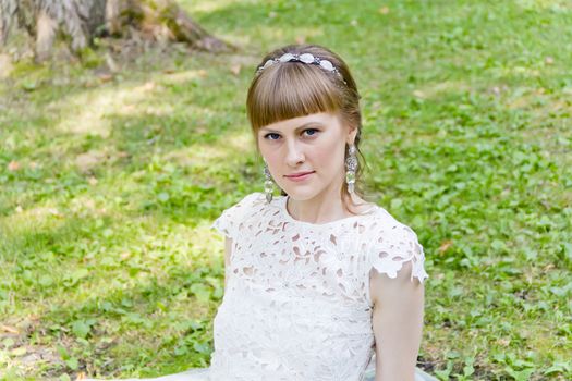 Beautiful bride in white dress sitting on the green grass