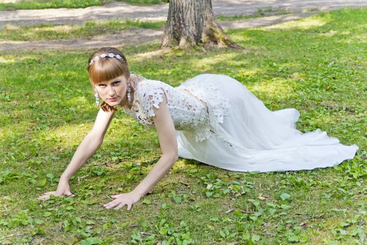 Bride in white lace dress crawl on green grass at the summer time
