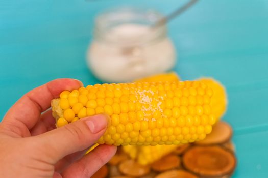 woman hand holding cooked corn on blue background