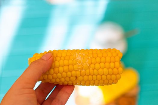 woman hand holding cooked corn on blue background