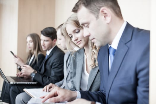 Business people working together sitting in a row in lobby and holding laptop and documents on knees