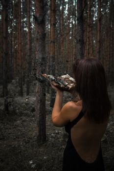 Halloween concept. Witch in black among the forest. Witchcraft and magic. Spell with a book. Photo for your design.