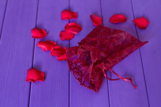 An organza pouch and petals on a purple wooden background