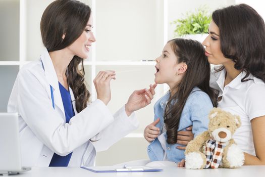 Little girl and her mother at pediatrician office. Doctor examine child's throat