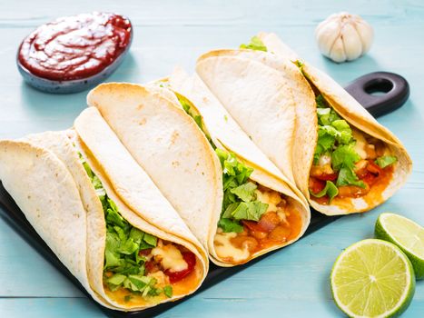 Three homemade tacos with chicken, vegetables and salsa. Latin food tacos on black wooden cutting board over blue wooden background