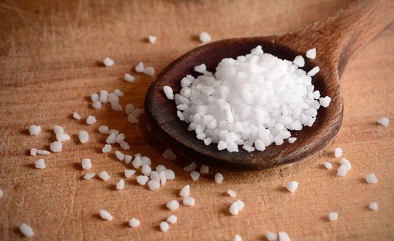 White clear salt crystals on a wooden spoon.