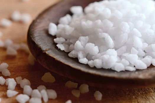 Macro shot of a white clear salt crystals on a wooden spoon.