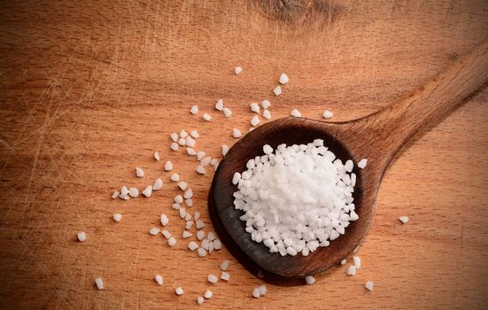 Top view of white clear salt crystals on a wooden spoon.