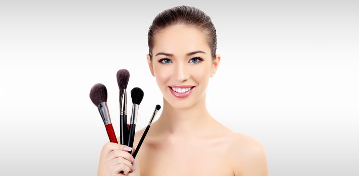 Pretty woman with makeup brushes against a grey background with copyspace