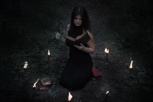Halloween concept. Fairy in black. In the witchy circle. With a book of spells in hand. Inserts the spell into the book.