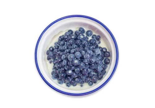 Top view of the dessert made of the fresh wild bilberries and sweetened condensed milk in the blue bowl on a white background
